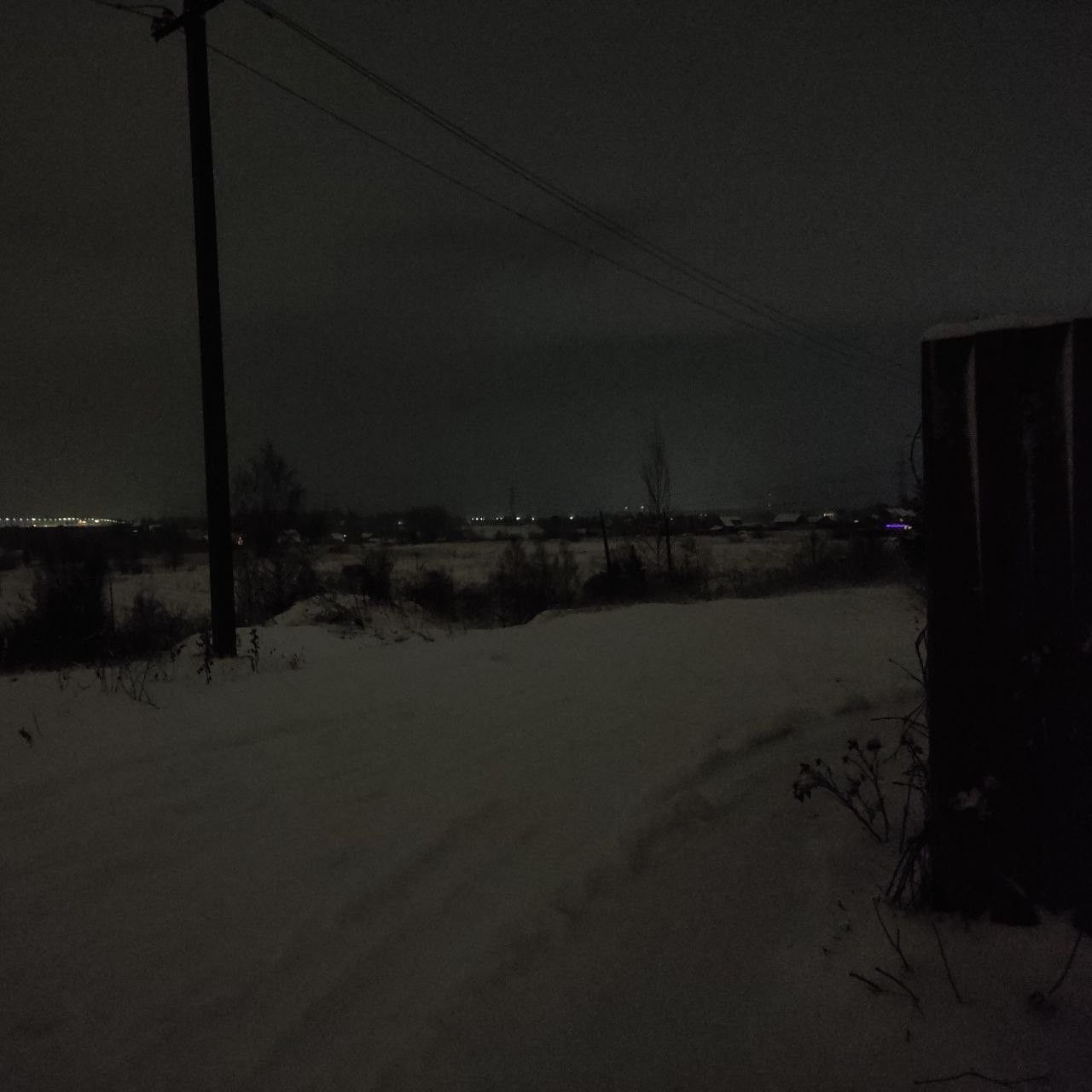 snow-covered field at night under heavy sky with distant horizon glow